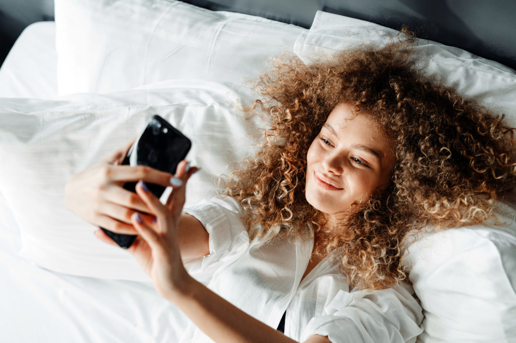 Girl with phone in bed, having virtual sex