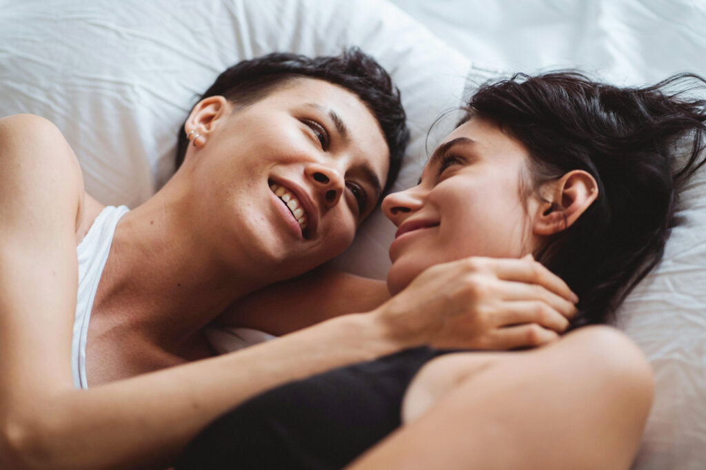 Lesbian women in bed, wondering how long to wait before having sex